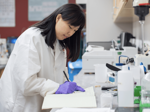 Bioengineer - a scientist in a lab coat and gloves writing in a notebook