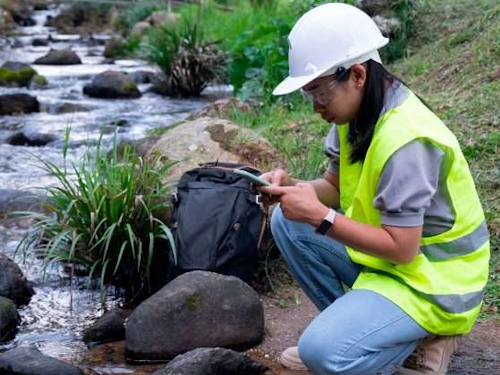 Environmental Engineer - a scientist in a hard hat and safety vest measuring water quality