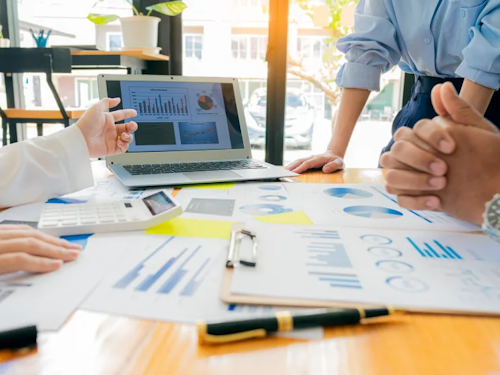 Health Policy Analyst - a meeting between three analysts with papers with graphs printed on them spread across a table