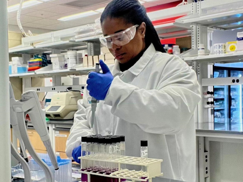 Microbiologist - a scientist in a lab coat, safety glasses, and gloves pipetting