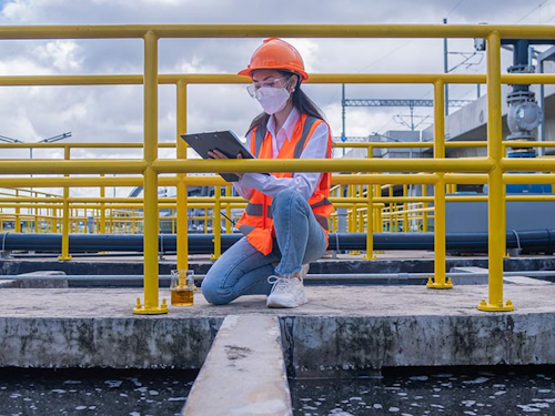 Public Health Engineer - a scientist in a hard hat and a safety vest writing notes about waste water